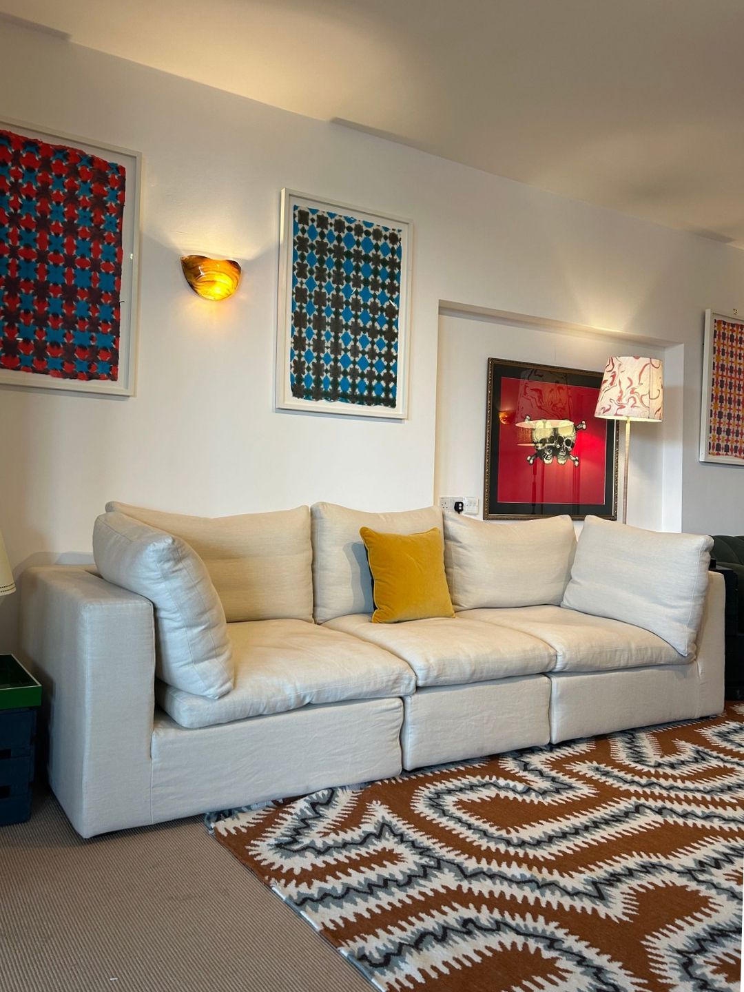 The Wee Bonnie sofa in light linen, styled with mustard yellow cushions, colourful framed artwork and a patterned rug in a living room setting.