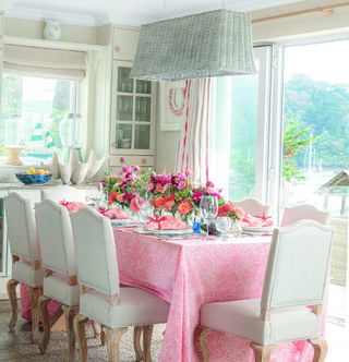dining area with dining table and white chairs and pink tablecloth and flowers and glass door
