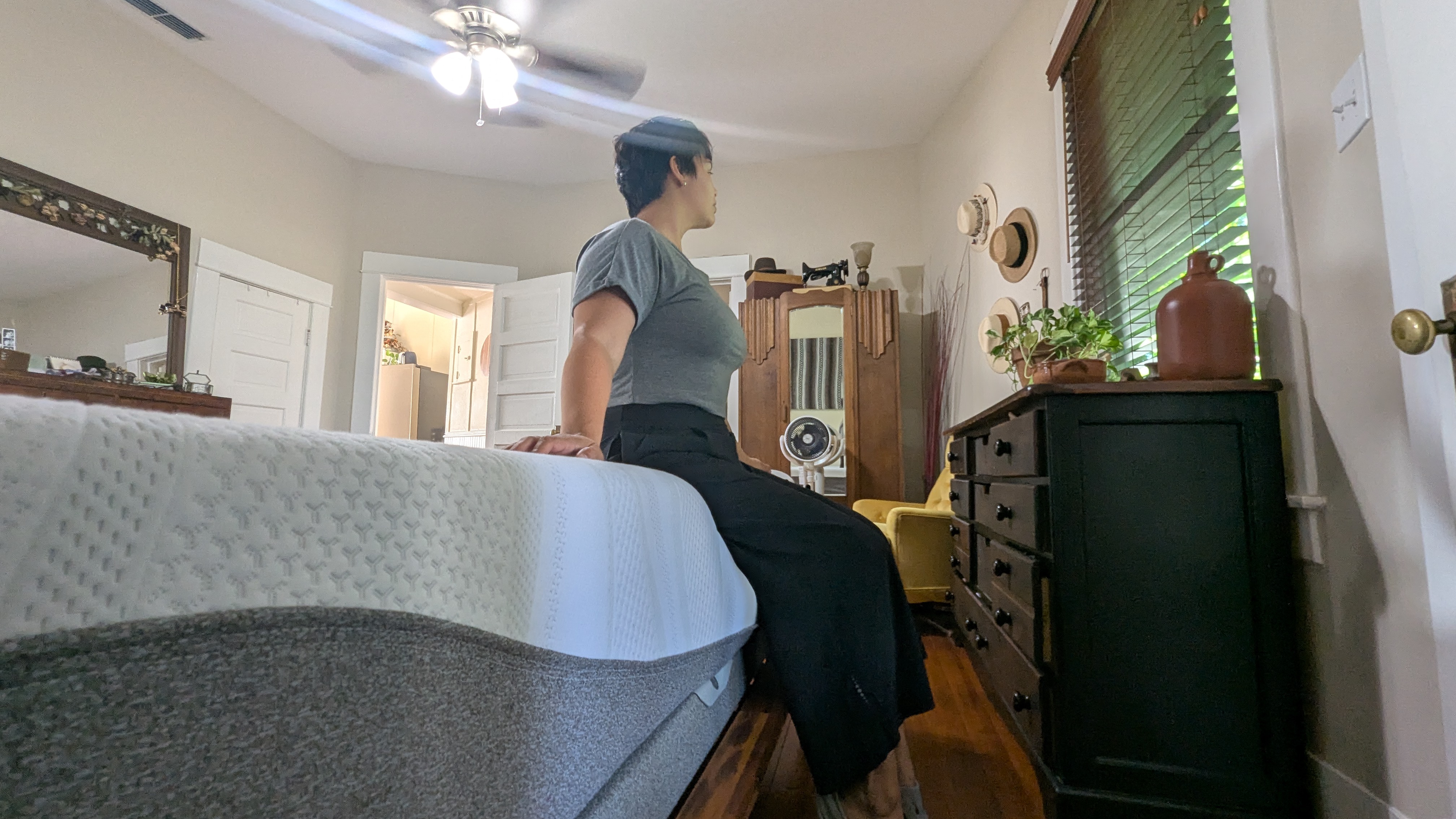 Mattress tester wearing grey top and black trousers sitting on edge of Sleep Number i8 smart mattress