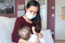 A mother wearing a mask while holding her baby.