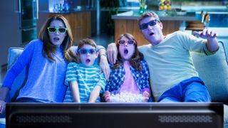 A family of four watches TV while wearing 3D glasses.