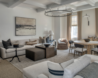 Neutral, contemporary living room space with cream couches, detailing on throw pillows, modern coffee table part-wood over fabric and round chandelier