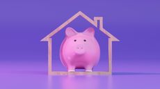A piggy bank inside the frame of a house against a purple background.