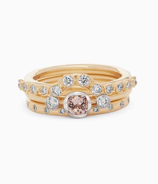 Gold engagement ring with pale red main stone and studded in diamonds on the band