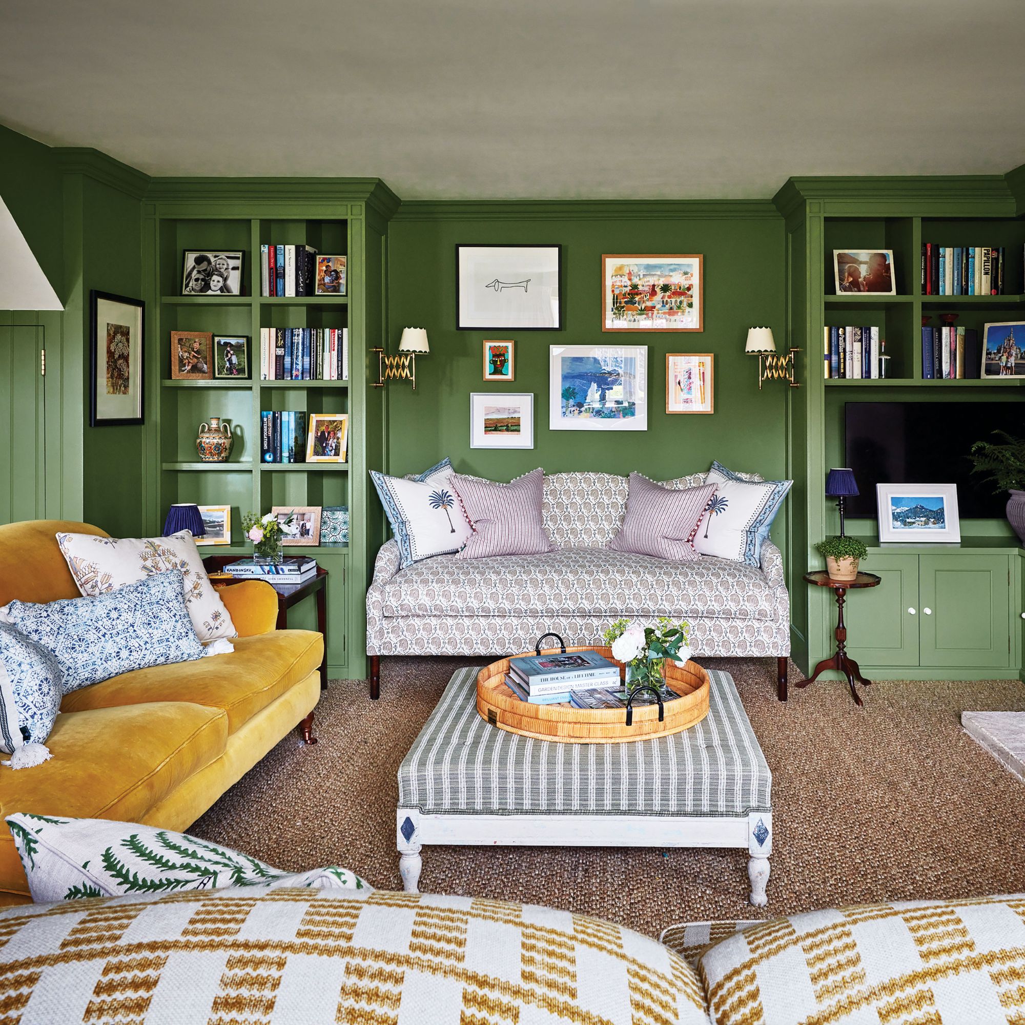 Family room painted in green, with 3 sofas and a lot of storage for books and photos