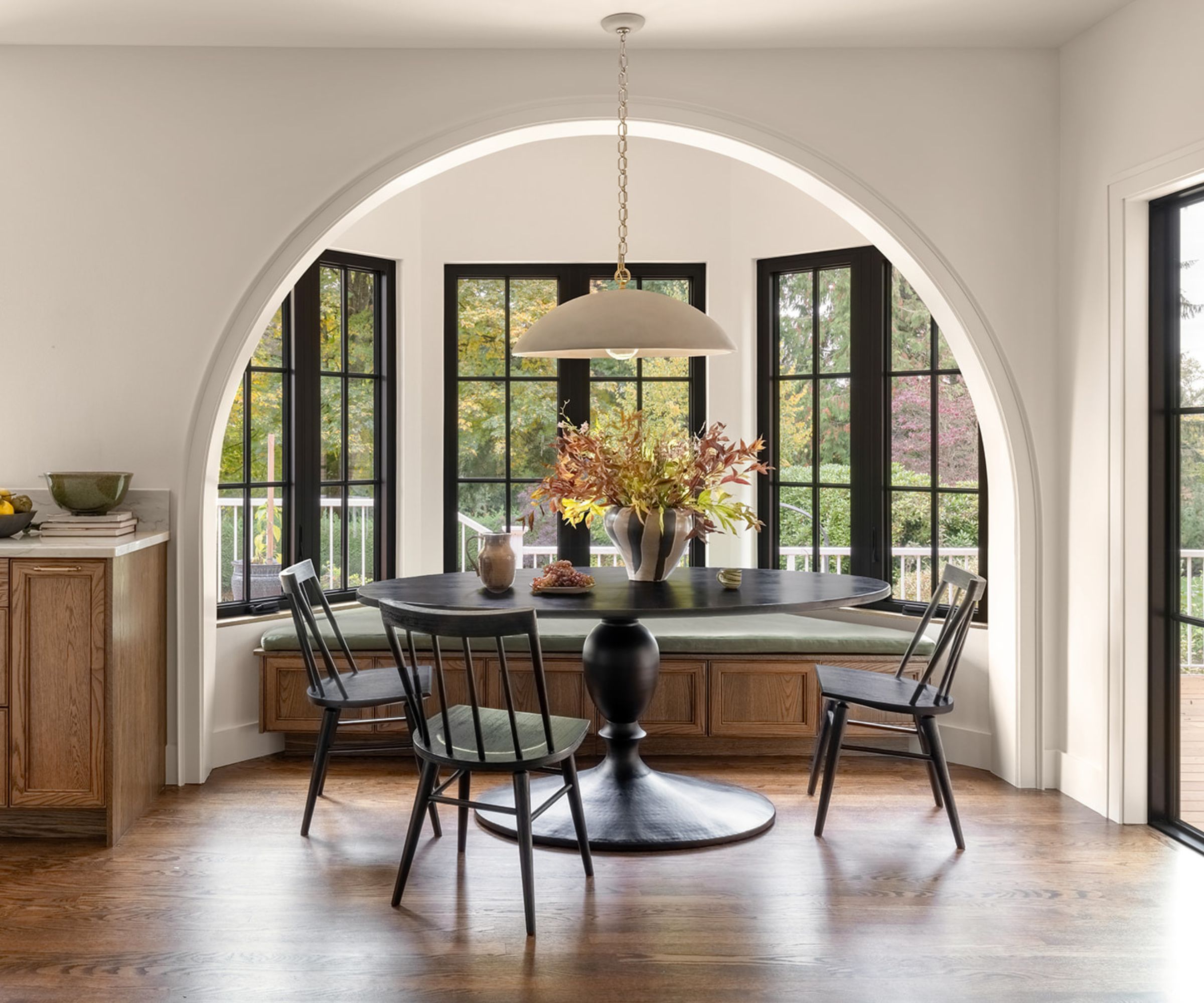 A wood and white kitchen with a large bay window transformed in to a dining nook with a banquette
