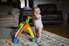 Portrait of happy baby girl with walker standing on rug at home 