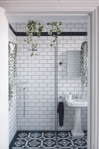Bathroom with black and white geometric pattern floor tiles, shower area, white wall tiles and pedestal basin.