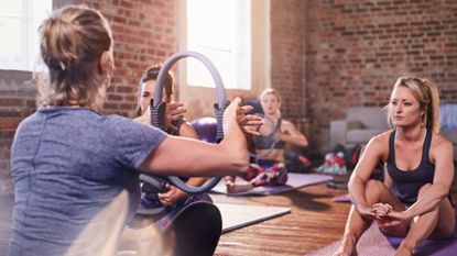 Women in fitness class facing teacher who holds up a Pilates ring