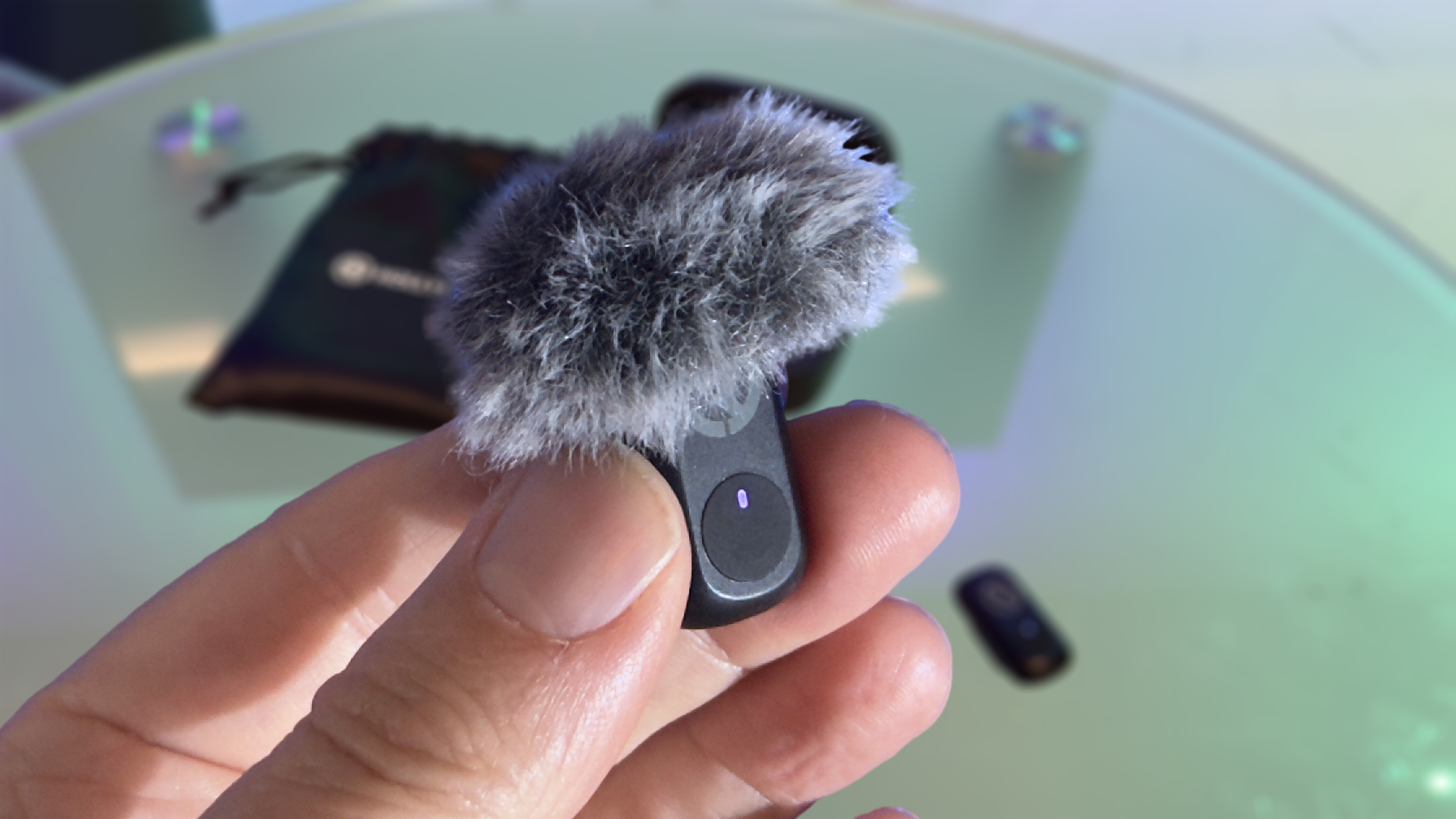 Close-up of a hand holding the transmitter mic. The mic is &amp;lsquo;wearing&amp;rsquo; a fluffy windshield