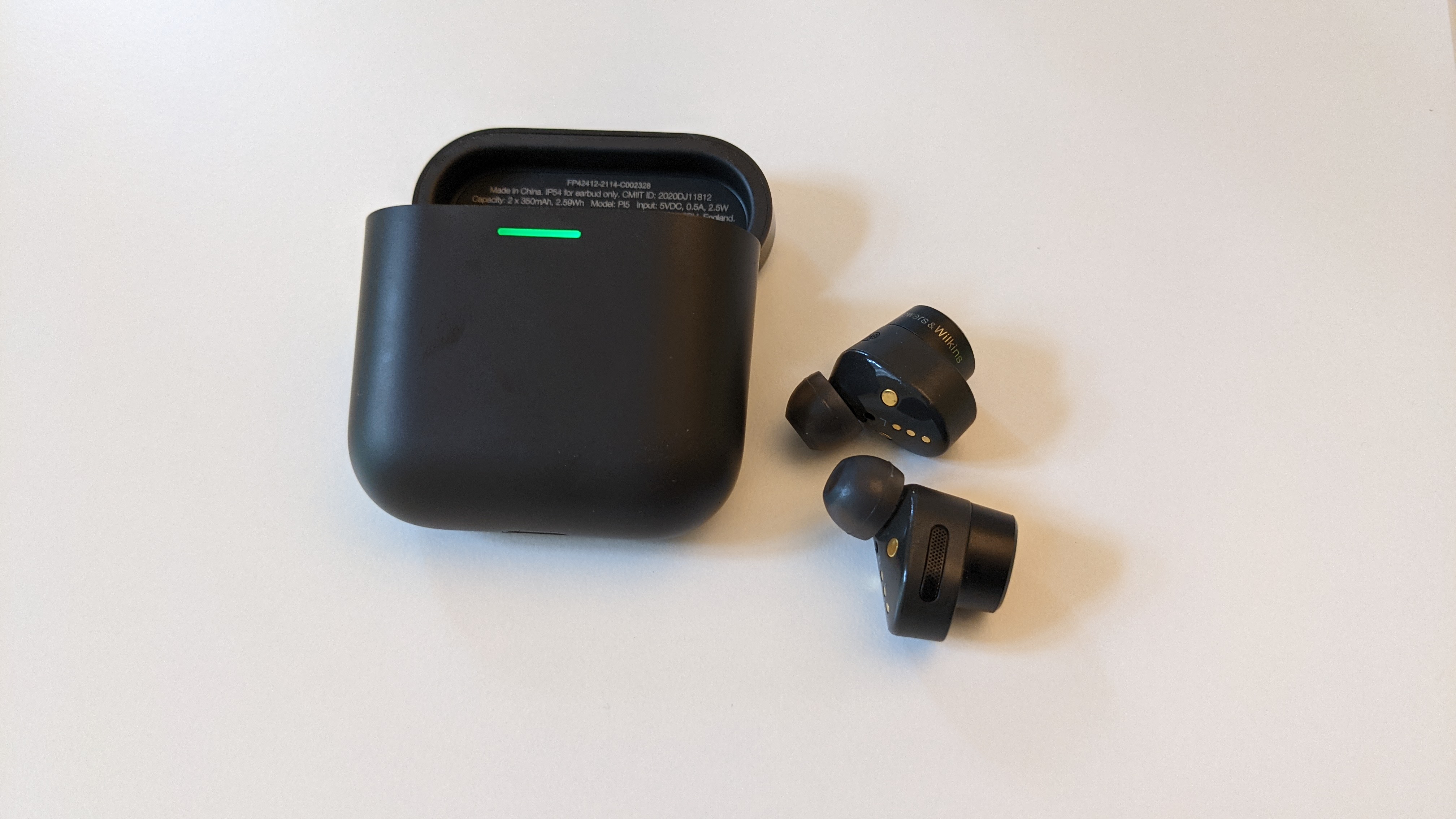 Anthrazitfarbene Bowers & Wilkins PI5 liegen neben dem Ladecase auf einem weißen Tisch