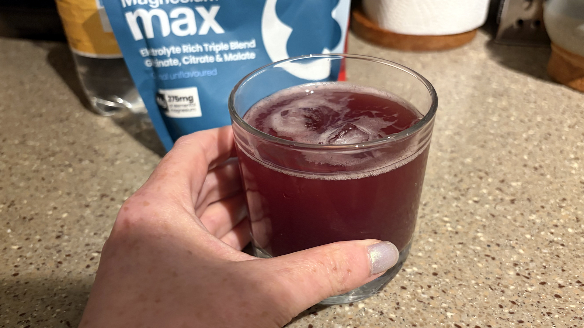 A close up of a hand holding a glass containing the sleepy girl mocktail. In the background, you can see a packet of powdered magnesium