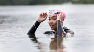 Woman holding goggles wearing wetsuit in pond