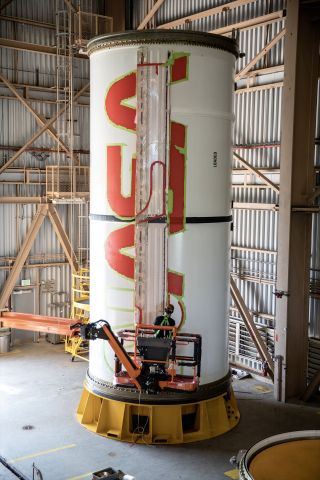A worker with NASA's Exploration Ground Systems finishes the first coat of the bright red "worm" logo taking shape on the side of an Artemis I solid rocket booster segment at Kennedy Space Center in Florida.