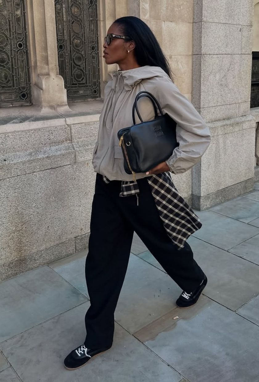 @nlmarilyn wears a beige technical jacket, black barrel-leg trousers, trainers and black leather bag
