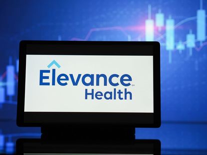 Elevance Health logo on tablet with blue stock chart blurred in background