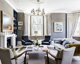 Grey living room ideas shown in a traditional scheme with dark blue armchairs and shelving as accents.