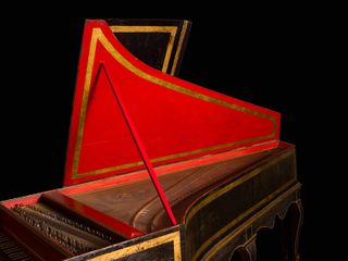 A wooden piano in brown, gold and red photographed against a black background