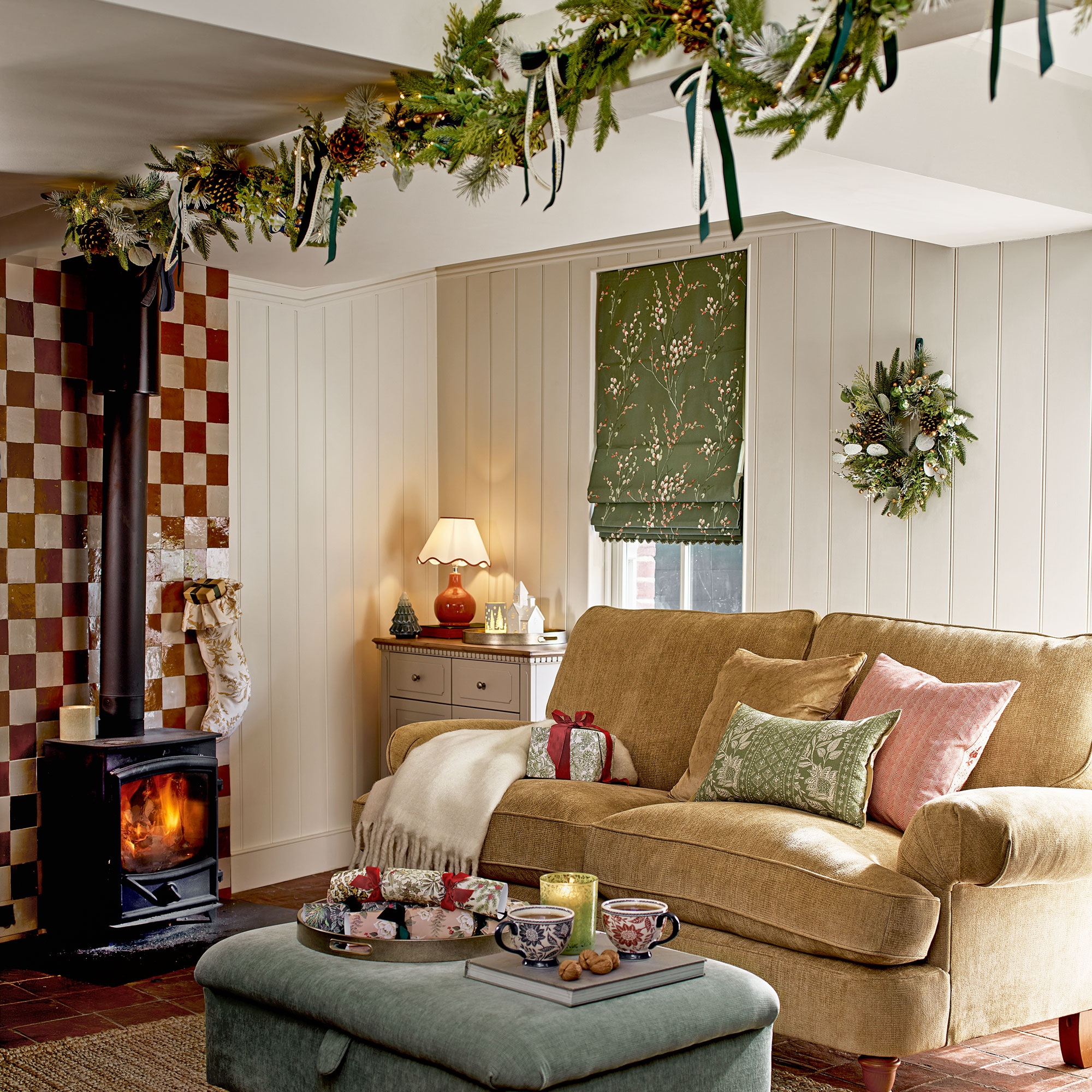 White panelled cottage style living room with a checker board tiled fireplace, yellow sofa, blue ottoman and a garland hung from the ceiling