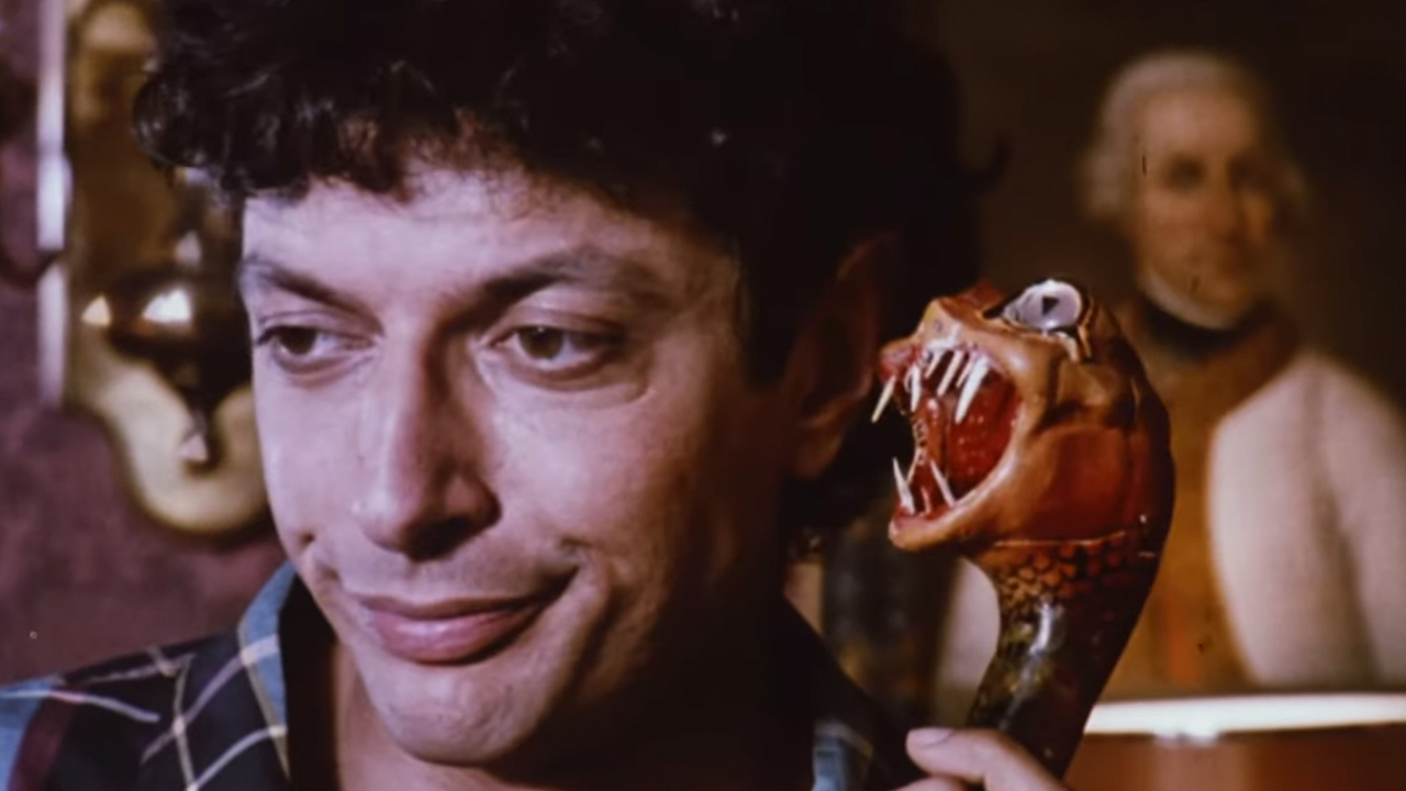 Jeff Goldblum smirking with a plastic snake with fangs next to him