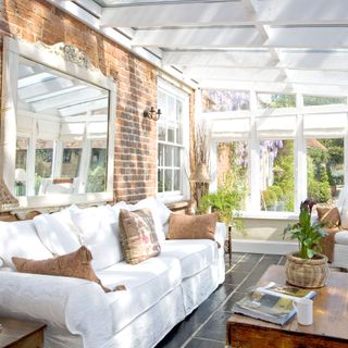 Small bright conservatory with large white sofa and exposed brick wall