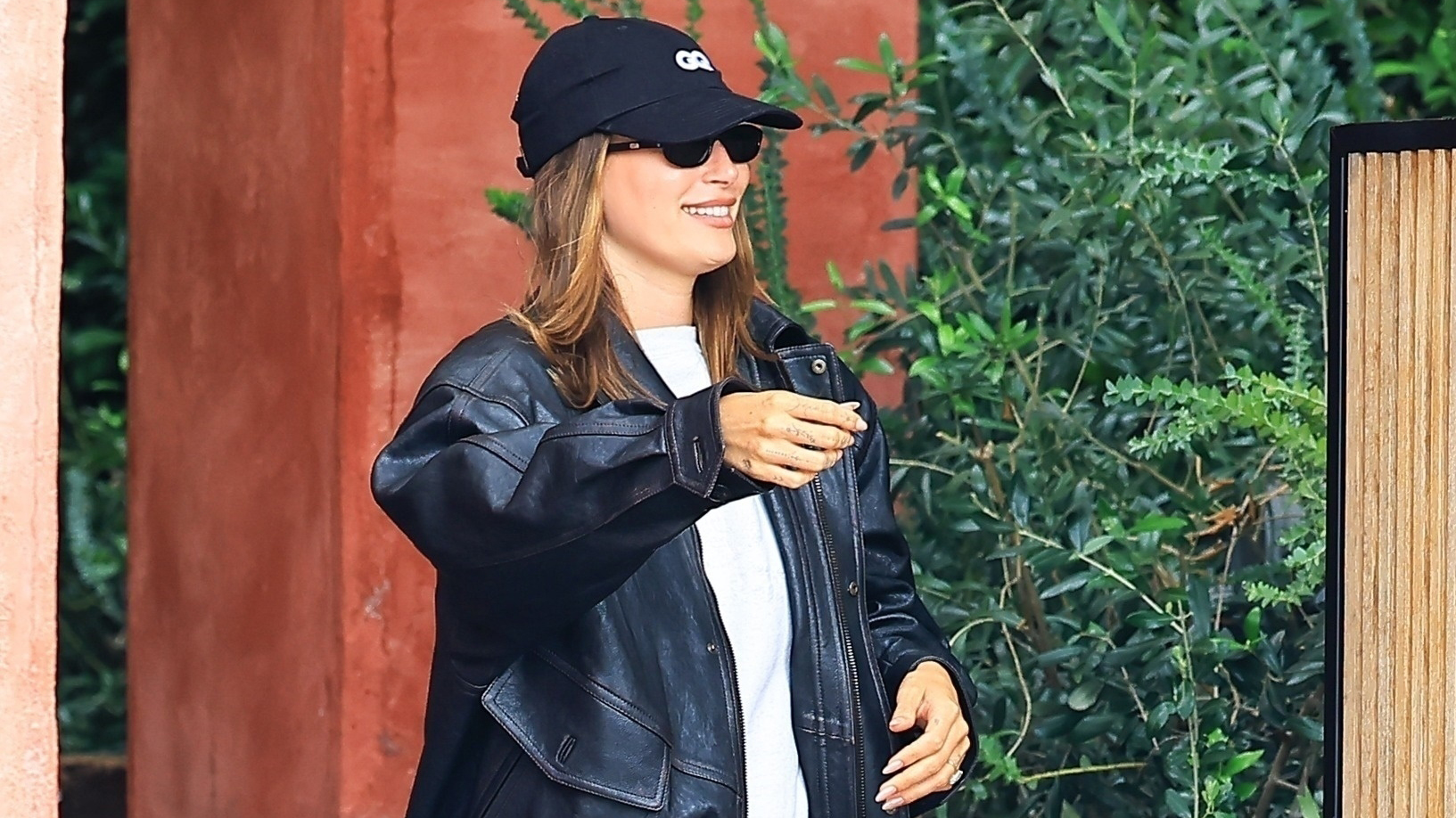 Hailey Bieber wearing a leather bomber jacket, white T-shirt, bike shorts, a baseball cap, white crew socks, and leopard-print loafers at Great White in West Hollywood