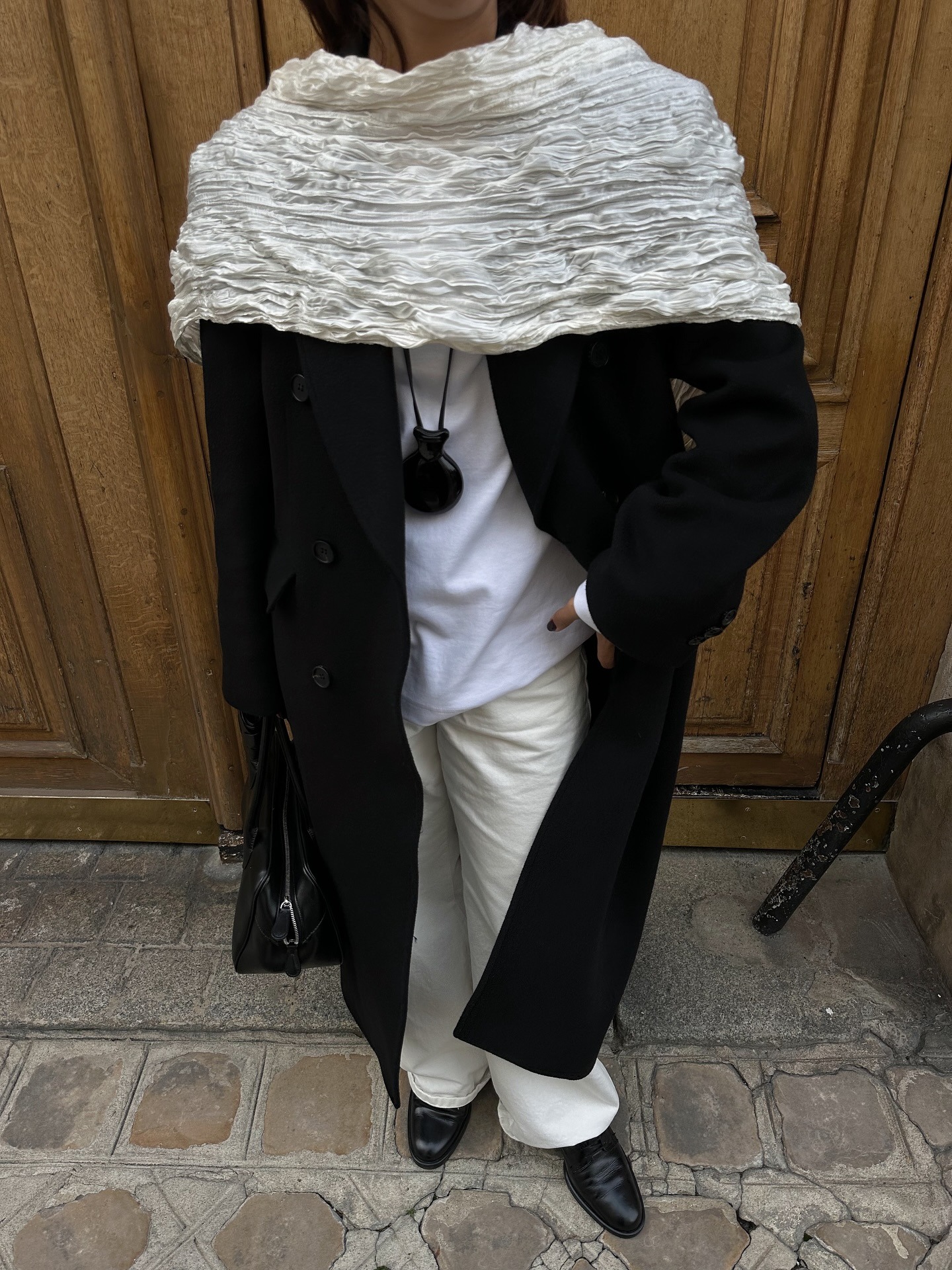 Woman wearing white jeans with black coat, white scarf, and black loafers.