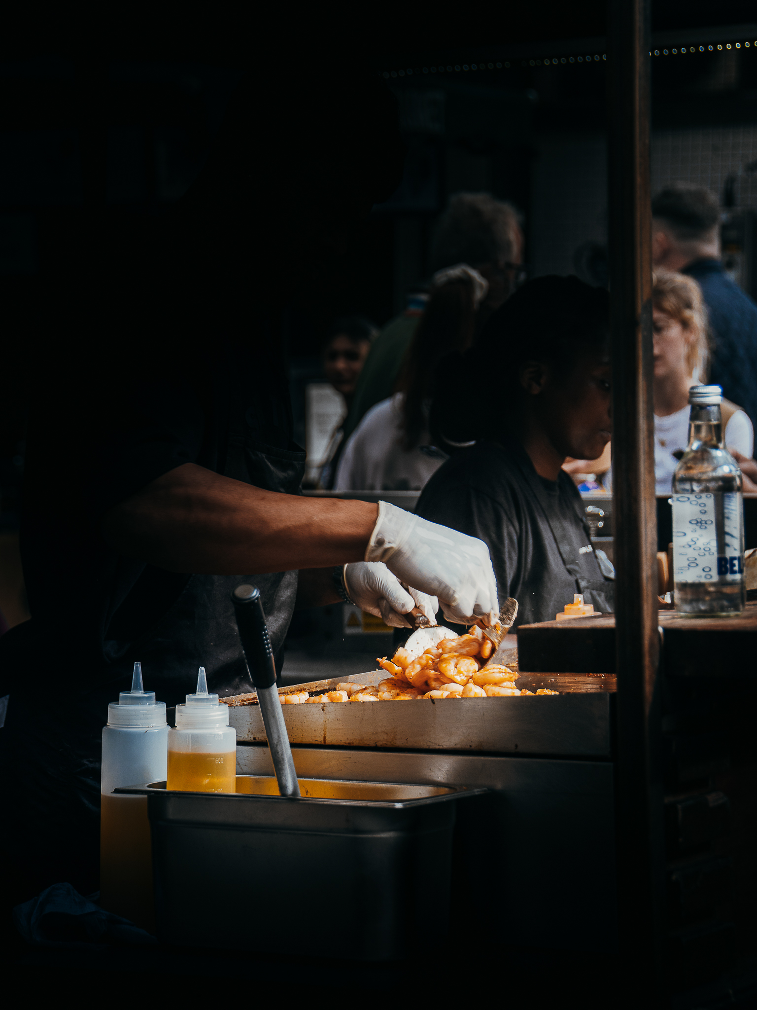 Street food vendor serving grilled shrimp at a busy market. The scene is dimly lit, with focus on the food