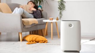 Air purifier in living room with a woman reading book on sofa