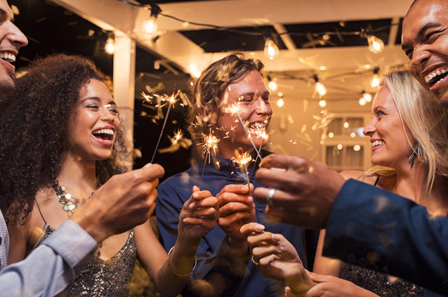 Three men and two women hold sparklers while laughing at a party