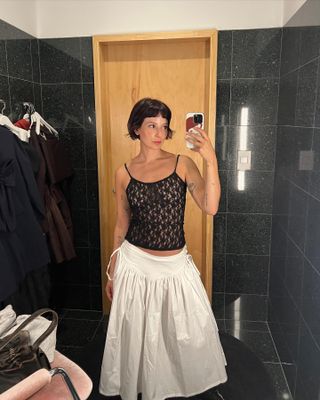 Woman wearing a black lace tank top and white poplin midi skirt.