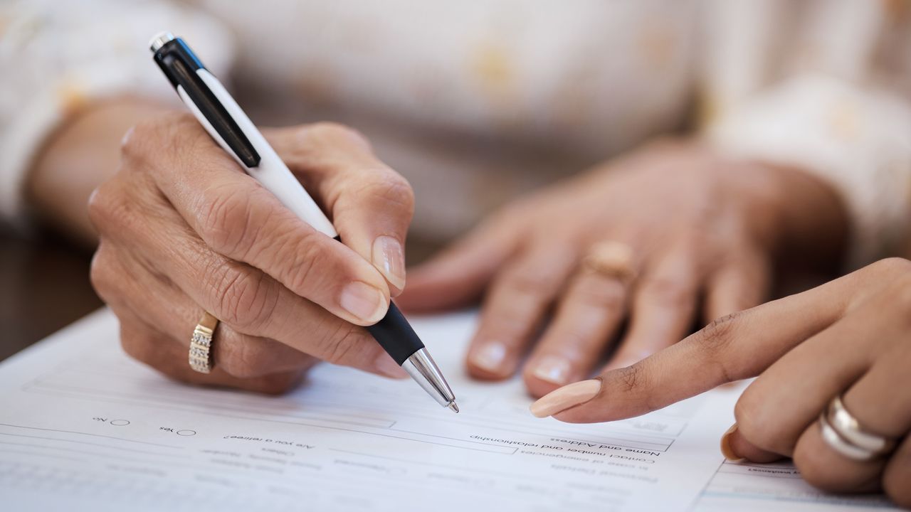 A woman signs estate planning documents, only her hands showing.