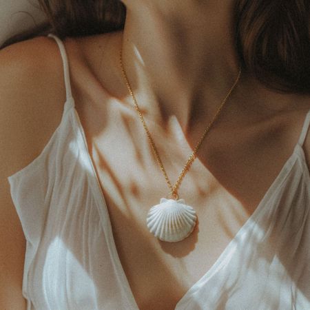 A woman's collarbones with a shell necklace and slip camisole top