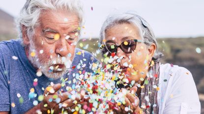 An older couple blows confetti out of their hands to celebrate how much they reduced their taxes in retirement.