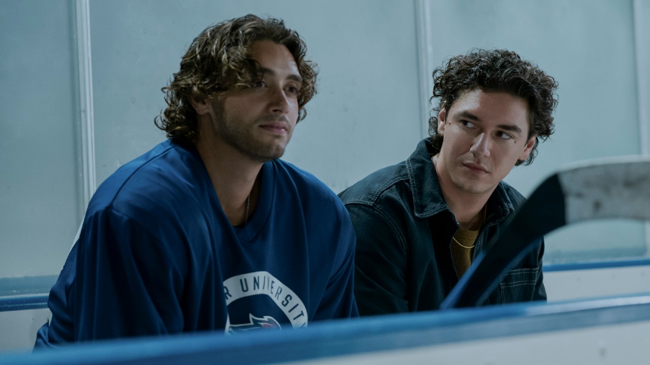 Logan in his hockey gear, and Garrett sitting next to him in normal clothes.