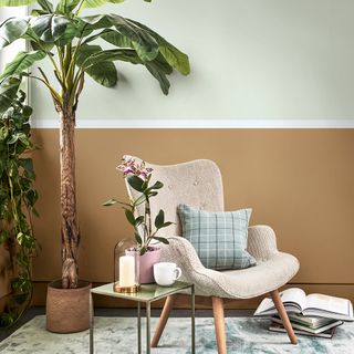 A cream armchair with a tartan cushion next to an indoor palm plant and white and brown wall