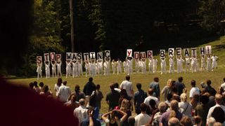 People dressed entirely in white hold up signs with letters that read "Stop Wasting Your Breath" in The Leftovers