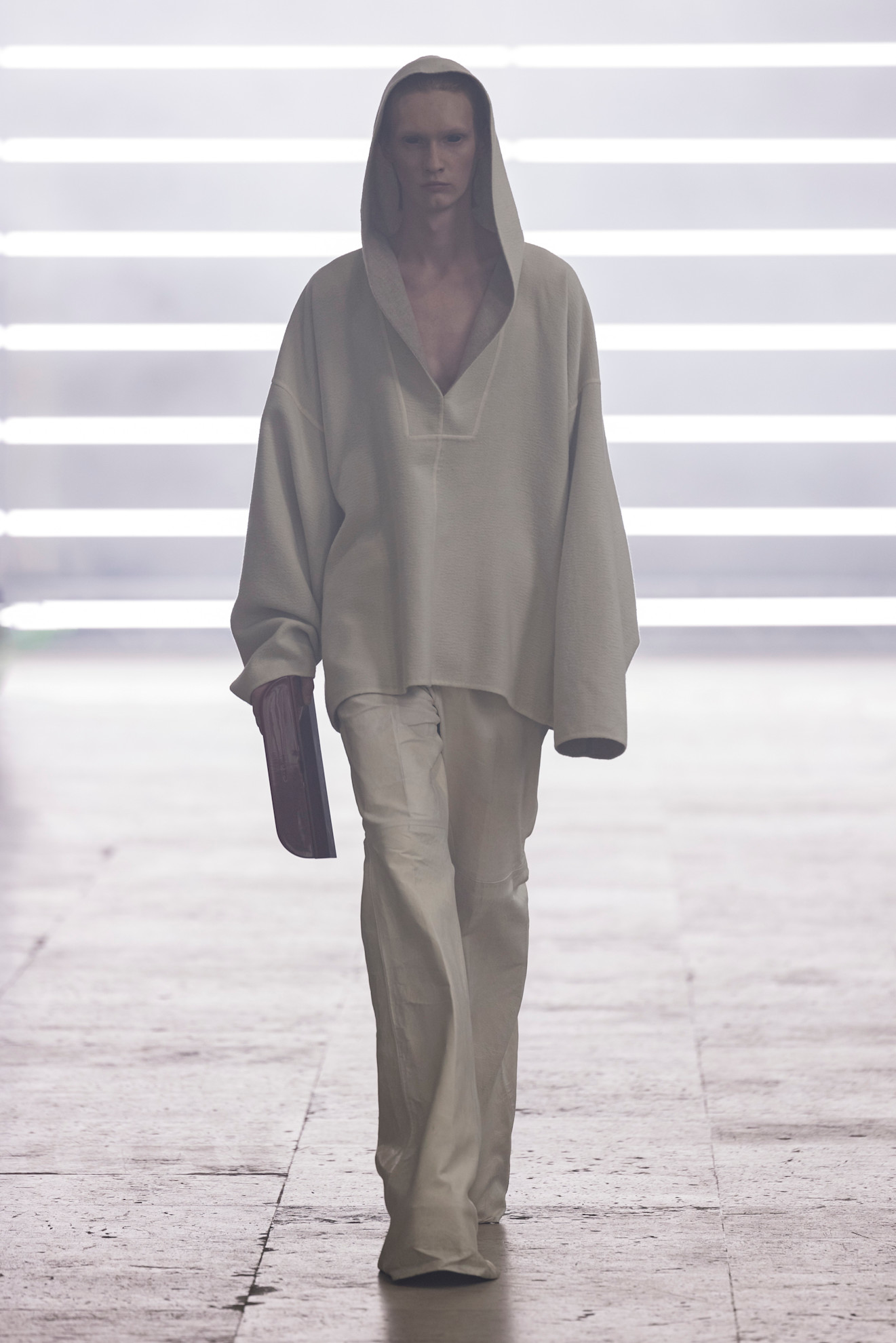 A model at the F/W 25 Rick Owens show wearing a hooded off-white pullover and flared wrinkle-effect pants.