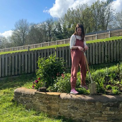 Woman holding spade, standing on stone wall