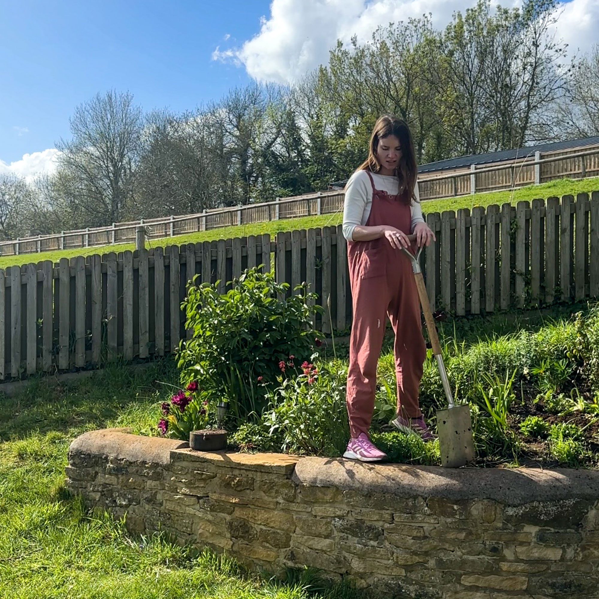 Woman holding spade, standing on stone wall
