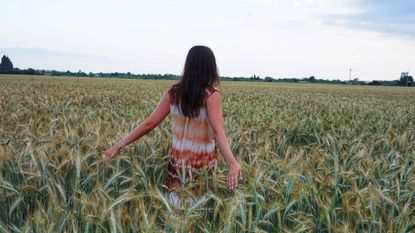 A woman runs her hands through wheat in a wheat field.