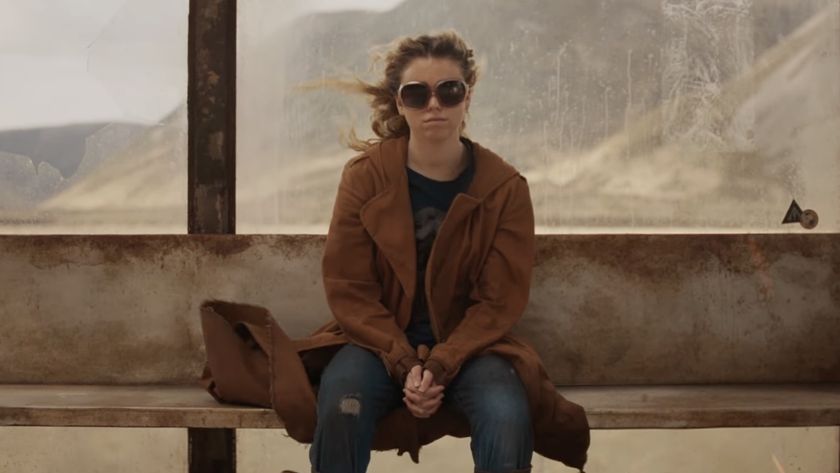 Milly Alcock's Kara wearing sunglasses and civilian clothing, seated at alien "bus stop" in Supergirl movie