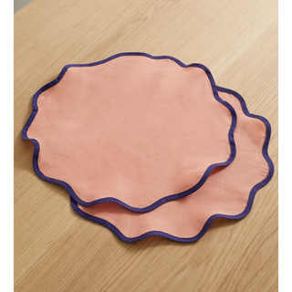 two pink linen placemats with a navy scalloped rim detail