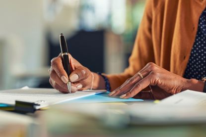 Close-up of woman signing documents at home using a pen.