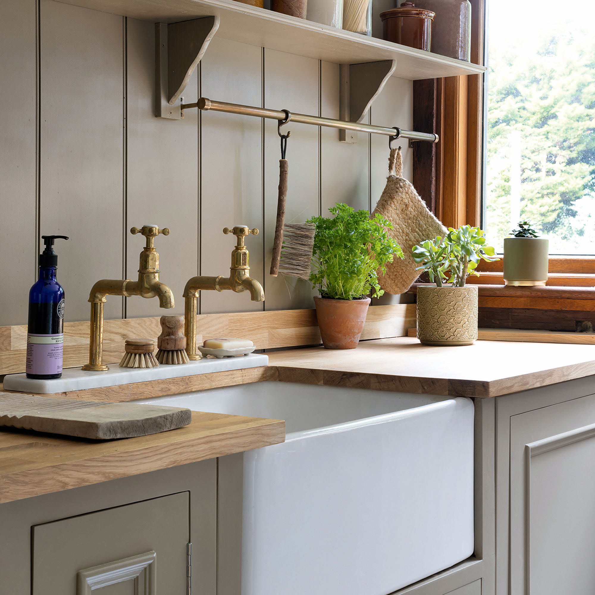 Green kitchen with an apron sink and brass taps with a wooden countertop