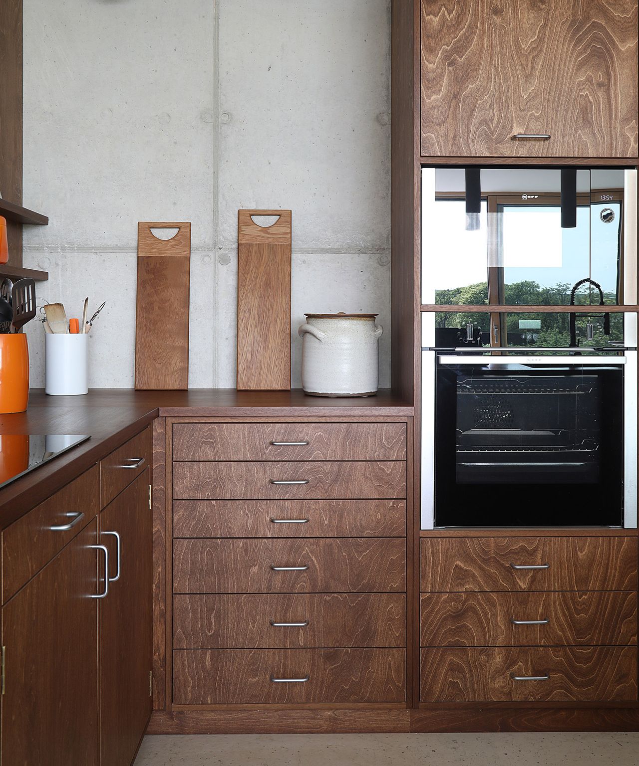 A dark wooden kitchen with metal handles. The oven is built in and there are pops of orange colour with the utensils pots