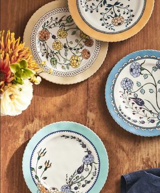 A birds eye shot of four circular plates with colorful floral patterns on them and a vase with yellow flowers