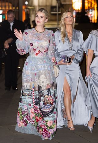 Lady Kitty Spencer waving and Lady Eliza Spencer walking, both wearing blue gowns outside at night