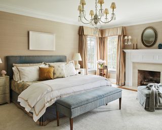 A bedroom with a blue upholstered bed and a storage bench, sand walls and white fireplace