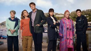 A shot of the main cast of Beyond Paradise season 2 with Shipton Abbott in the background. From left to right: Barbara Flynn as Anne Lloyd, Sally Bretton as Martha Lloyd, Kris Marshall as DI Humphrey Goodman, Zahra Ahmadi as DS Esther Williams, Felicity Montagu as Margo Martins, and Dylan Llewellyn as PC Kelby Hartford